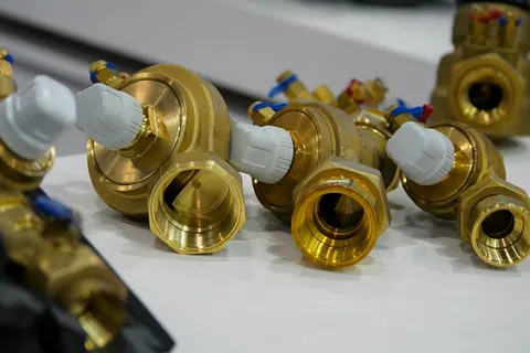 Close-up of brass plumbing valves with white plastic knobs arranged on a white surface.