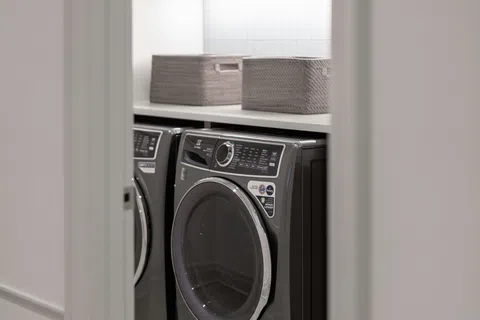 Modern laundry room with front-loading washer and dryer, countertop with woven baskets, gray cabinets, and tiled floor.