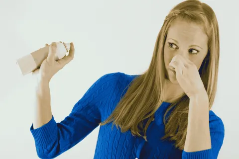 Woman in blue sweater pinching nose with one hand and holding spray can in other hand
