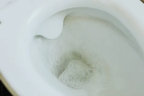 Close-up of a toilet bowl flushing with water swirling and bubbles inside the bowl.