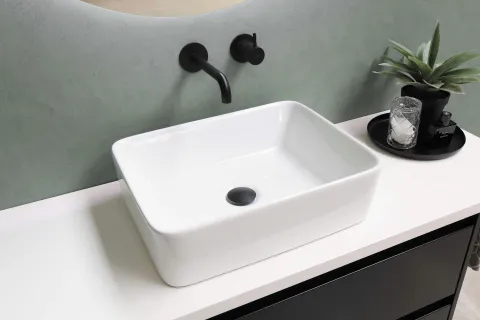Modern rectangular white bathroom sink with matte black faucet and accessories on white countertop