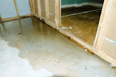 Water flooding an unfinished basement with exposed wooden framing and concrete floor