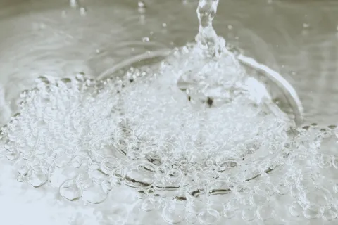 Close-up of clear water droplets and bubbles forming as water splashes on a smooth surface.