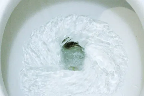 Water swirling rapidly down a white toilet bowl drain in a circular motion.