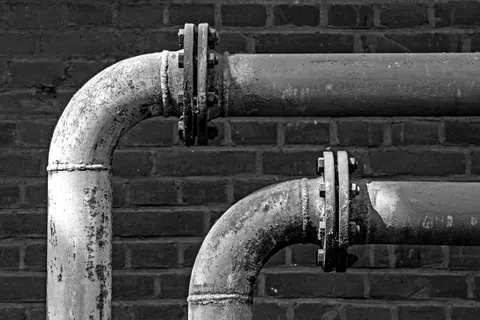 Close-up of two old metal pipes with flanges against a dark brick wall in black and white.