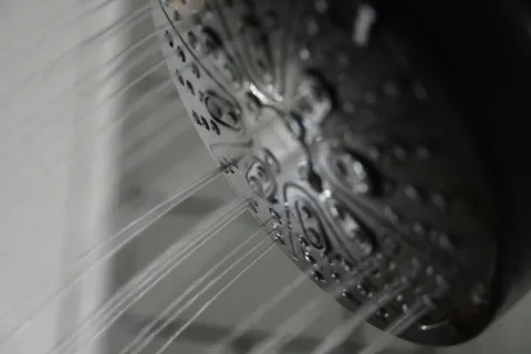Close-up of water streams flowing from a metallic showerhead with multiple spray nozzles in a bathroom.