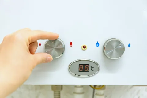 Hand adjusting temperature control knob on water heater with digital temperature display showing 8.8°C.