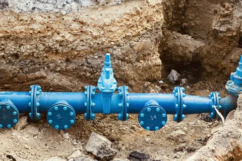 Blue underground water pipeline with valves installed in a trench surrounded by soil and rocks.