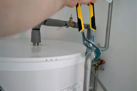 Person using adjustable wrench to tighten pipe connection on white water heater tank in utility room