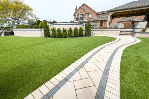 Curved stone pathway through well-manicured green lawn leading to a brick house with garden and shrubs.