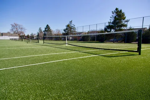 Empty outdoor tennis court with green artificial grass under a clear blue sky on a sunny day