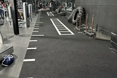 Gym workout area with sled push track, large tires, weight machines, and rubber flooring for functional training.