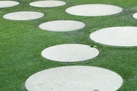 Circular concrete stepping stones arranged on green grass forming a pathway outdoors.