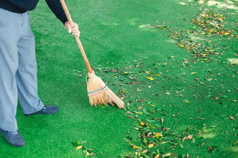 Person sweeping leaves off green artificial grass lawn with a broom.