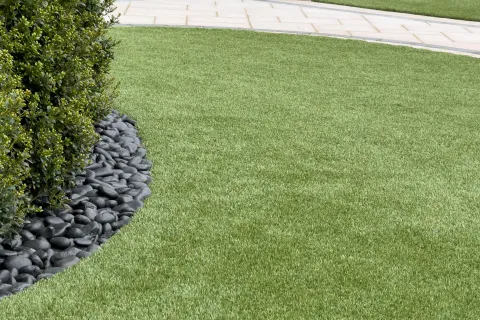 Well-manicured lawn with decorative black stones and green shrubbery along a tiled patio area.
