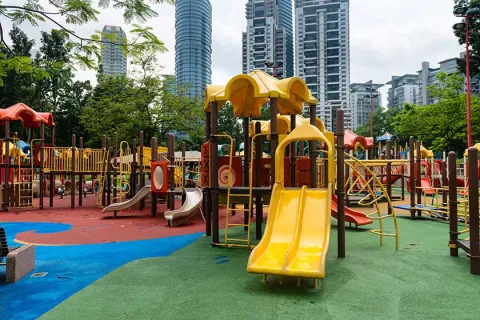 Colorful playground with slides and climbing structures in urban park surrounded by tall buildings and greenery.