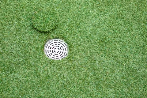 Close-up of a golf putting green with a drain and a golf hole surrounded by artificial grass.