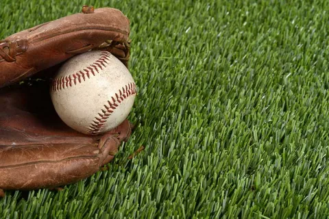 Baseball glove holding a ball resting on vibrant green artificial grass turf