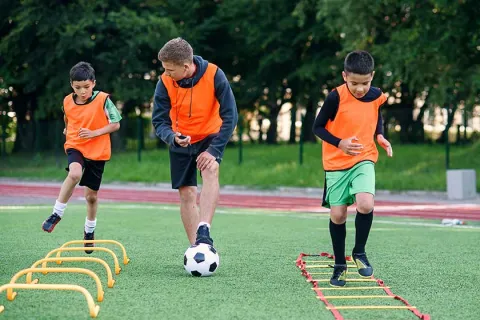 Coach and two boys in orange vests practicing agility drills on a soccer field during training session.