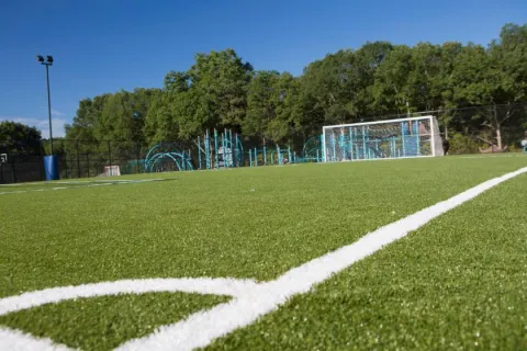 Green artificial turf soccer field with white boundary lines and goalpost under clear blue sky.