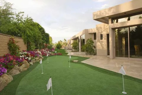 Well-manicured backyard with golf putting green and colorful flower beds under a cloudy sky.