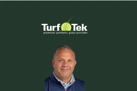 Portrait of a middle-aged man in blue jacket below Turf Tek synthetic grass provider logo on dark green background