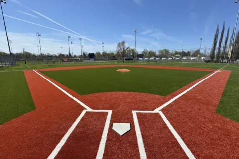 View of a well-maintained baseball field with home plate, batter's box, pitcher's mound, and clear blue sky.