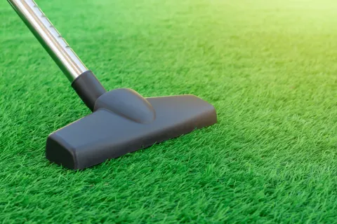 Vacuum cleaner head resting on bright green artificial grass under sunlight.