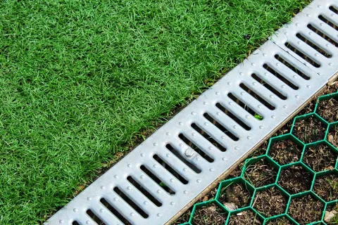 Metal drainage grate between artificial grass and hexagonal garden soil reinforcement grid