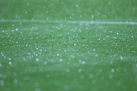Close-up of green grass field with white hailstones scattered and falling during a hailstorm