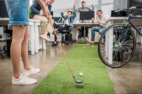 Office workers enjoying a mini golf setup in a creative workspace with artificial grass.