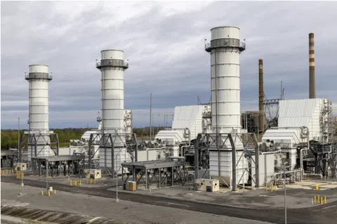 Industrial power plant with large white cooling towers and complex machinery under a cloudy sky.