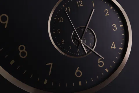Close-up of a black clock with gold numbers and hands, featuring a recursive spiral clock design.