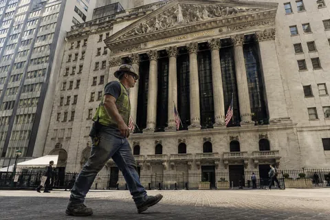 Construction worker walking past the New York Stock Exchange building with American flags and tall columns.