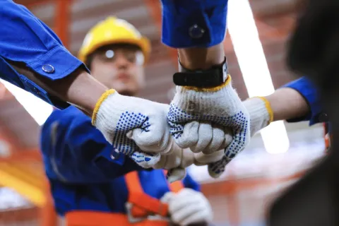 Construction workers in blue uniforms and gloves performing a group fist bump in an industrial setting