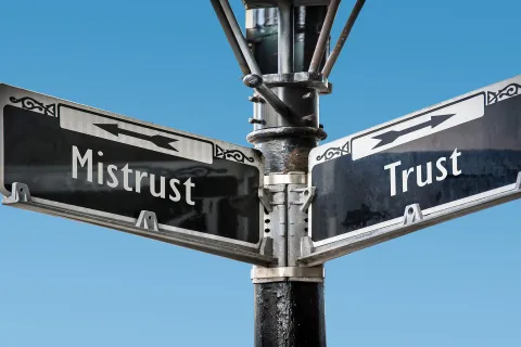 Black and white signpost with arrows pointing in opposite directions labeled Trust and Mistrust against a clear blue sky.