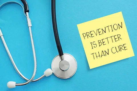 Stethoscope beside sticky note reading Prevention is better than cure on blue background.