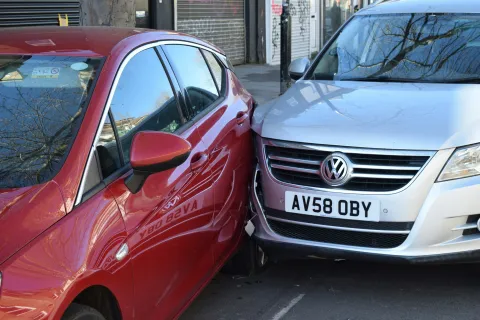 Red and silver cars involved in a close side-swipe collision on an urban street with visible damage.