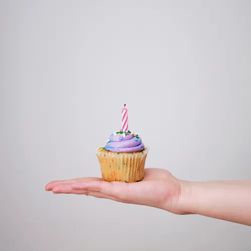 a hand holding a cupcake with a candle on top