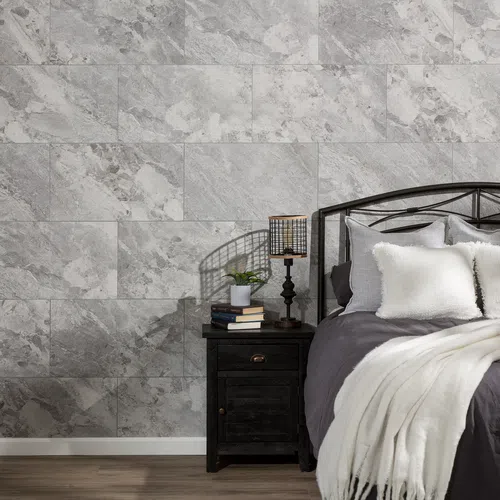 Cozy bedroom corner with metal bed frame, gray bedding, white pillows, wooden nightstand, lamp, and stone-textured wall.