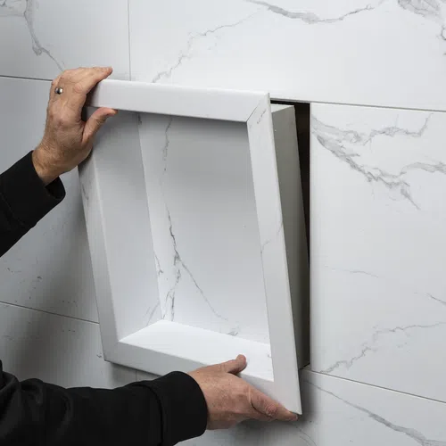 Person installing a white recessed wall niche with marble-patterned tiles surrounding the opening.