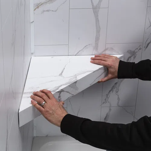 Hands installing a white marble-patterned corner shelf on a tiled wall in a bathroom or kitchen corner.