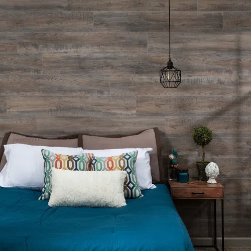 Modern bedroom with teal bedding, decorative pillows, wooden nightstand, small plant, and hanging geometric light.