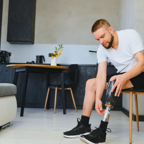 Man with a prosthetic leg sitting on a chair in a modern kitchen adjusting his shoe.
