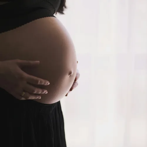 Close-up of a pregnant woman gently holding her belly wearing a black outfit with soft natural light background.
