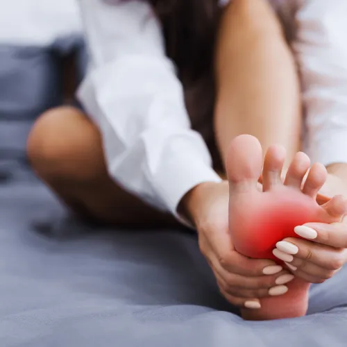 Person holding foot with red highlighted pain area on sole indicating discomfort or foot pain relief.