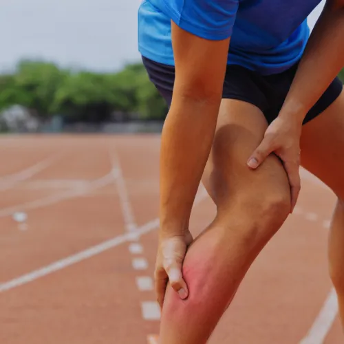 Runner clutching calf muscle in pain on outdoor track, highlighting muscle strain or cramp injury.