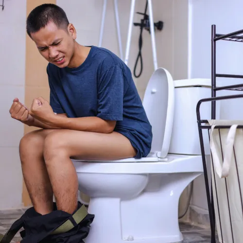 Man sitting on toilet in bathroom showing discomfort and pain holding his abdomen.
