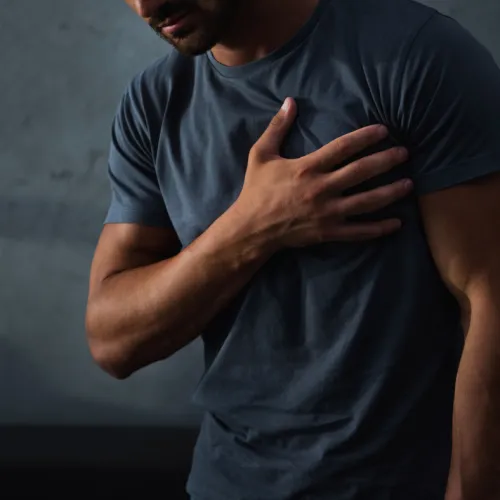 Man in dark shirt clutching chest in pain against a dark, textured background, suggesting heart discomfort or distress.