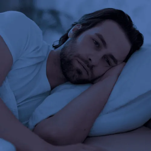 Man lying awake in bed at night, resting head on pillow, appearing restless and sleepless.